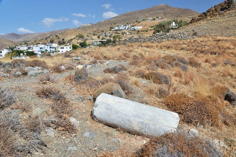 Le vestige d'une colonne grecque antique, posé par terre dans la nature face à la montagne