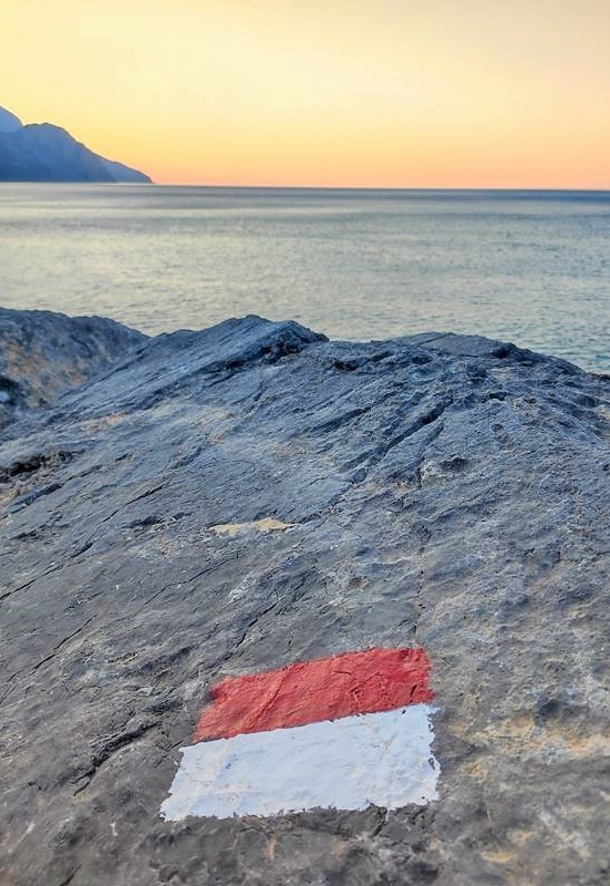 Une balise du sentier de randonnée E4 peinte sur un rocher, face au lever du soleil à Sougia (Crète)