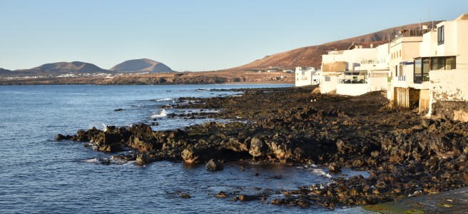 Maisons blanches du village d'Arrieta sur une coulée de lave face à la mer, volcans en arrière-plan